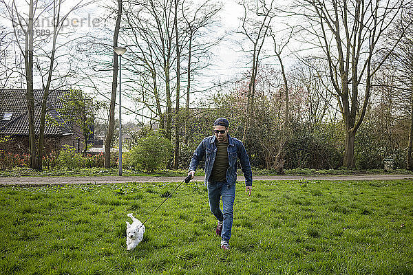 Lächelnder Mann läuft mit Hund auf Gras im Hof