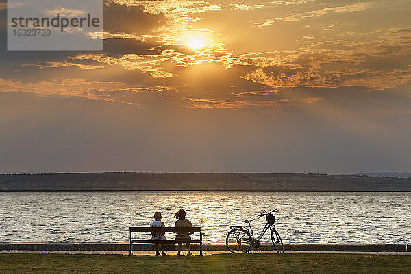 Österreich,  Burgenland,  Illmitz,  Neusiedler See,  Menschen auf Bank sitzend bei Sonnenuntergang