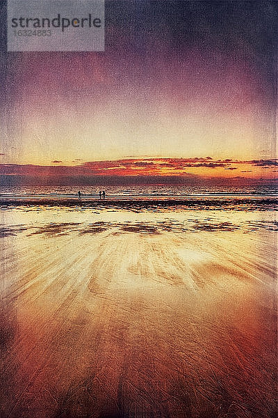 Drei Spaziergänger am Strand bei Sonnenuntergang
