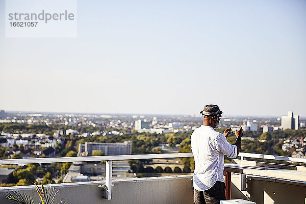 Älterer Mann,  der ein Foto macht,  während er sein Smartphone benutzt und auf der Terrasse eines Gebäudes steht