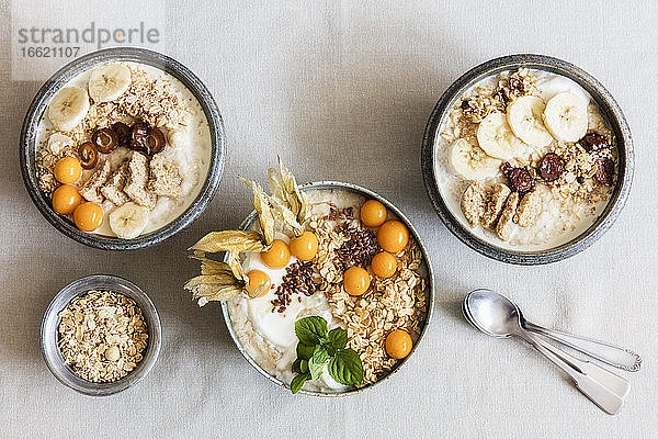 Drei Schalen Porridge mit Haferflocken,  Leinsamen,  Winterkirschen und Bananen