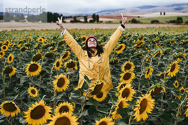 Junge Frau steht in einem Sonnenblumenfeld und macht Gesten für den Frieden