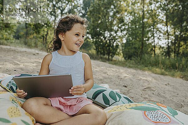 Lächelndes süßes Mädchen,  das wegschaut und ein digitales Tablet hält