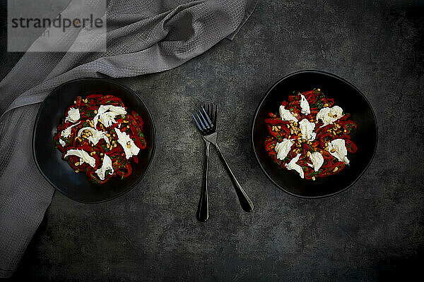 Zwei Schalen vegetarischer Salat mit roter Paprika,  Mozzarella,  gerösteten Pinienkernen,  Petersilie und Schnittlauch