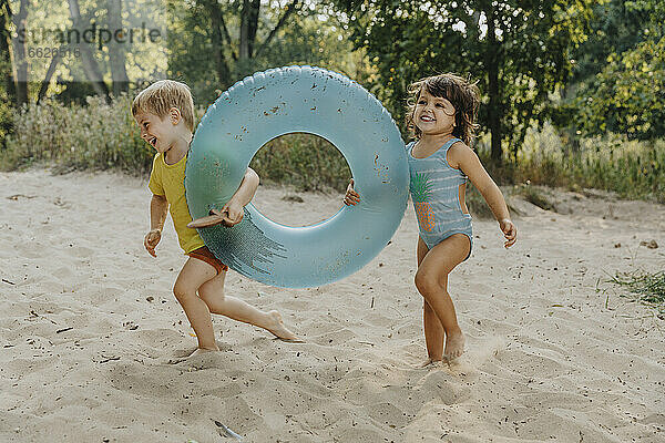 Kinder laufen mit aufblasbarem Ring am Strand