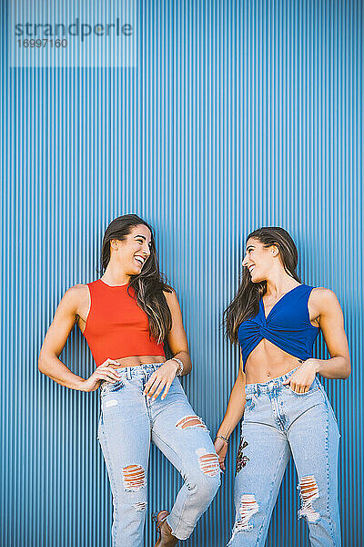 Lachende Zwillinge vor einer blauen Wand