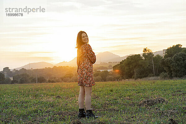 Glückliche junge Frau,  die bei Sonnenuntergang auf dem Lande steht