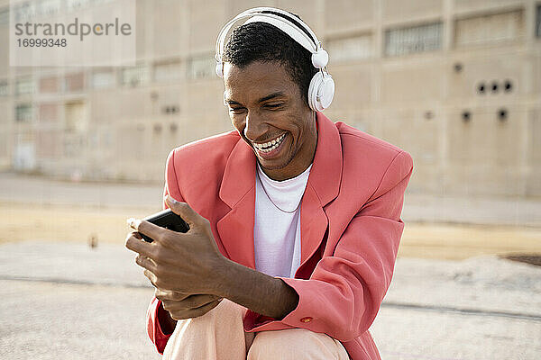 Glücklicher Mann mit Kopfhörern und Mobiltelefon im Freien sitzend