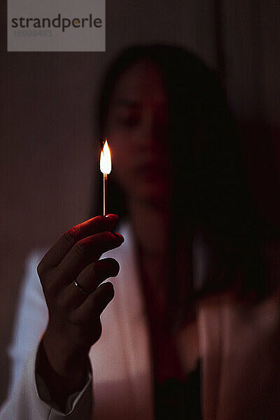 Frau steht und hält brennendes Streichholz im Dunkeln zu Hause