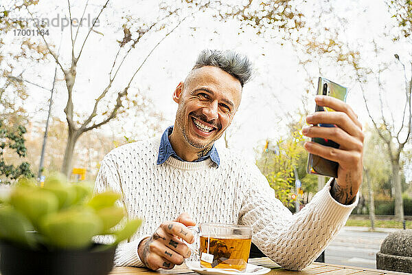 Glücklich mit Smartphone beim Tee im Straßencafé