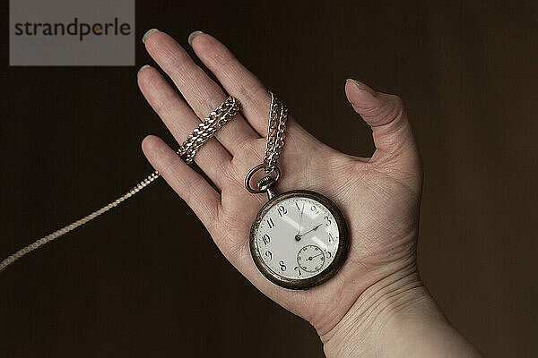 Die Hand einer Frau hält eine antike Taschenuhr