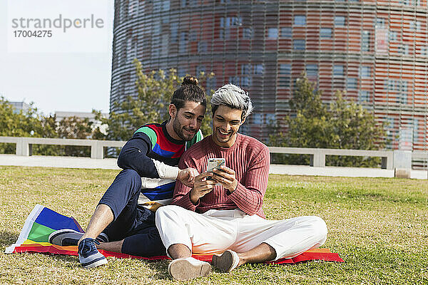 Lächelnder Mann mit schwulem Partner,  der im Park ein Mobiltelefon benutzt