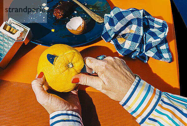 Hände einer älteren Frau,  die eine Orange mit einem Tafelmesser schält