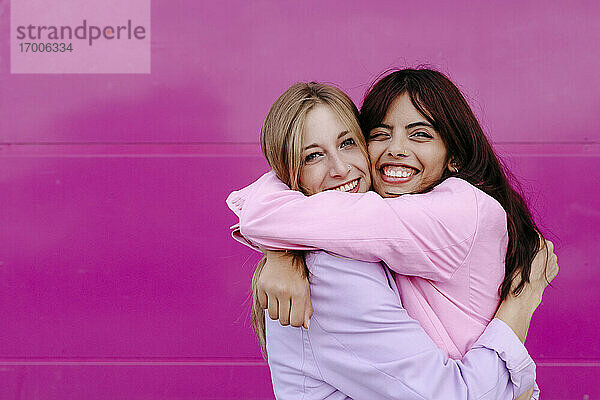 Glückliche Schwestern umarmen sich an einer rosa Wand