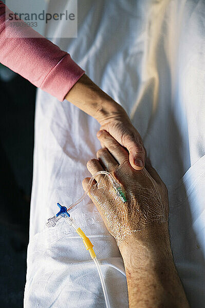 Frau hält Hand eines Patienten auf dem Bett im Krankenhaus
