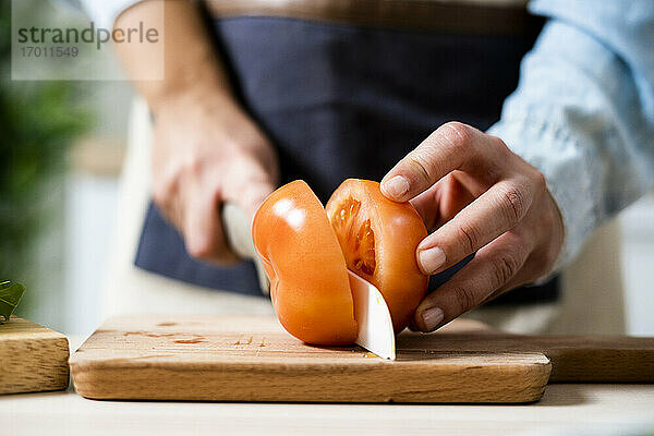 Die Hände einer Frau,  die eine Tomate auf einem Schneidebrett schneidet