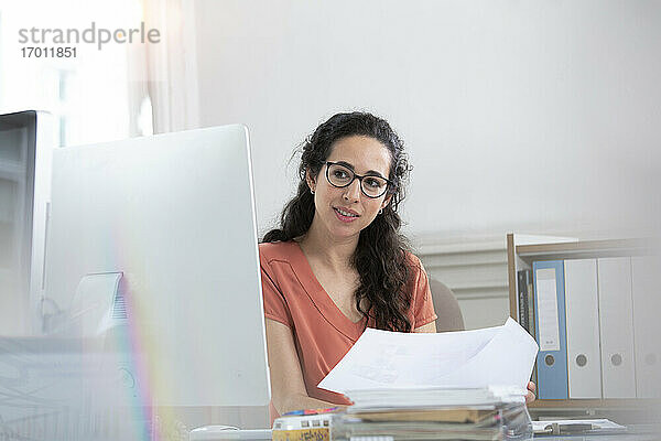 Weibliche Fachkraft,  die ein Papierdokument hält und auf einen Computer im Büro schaut