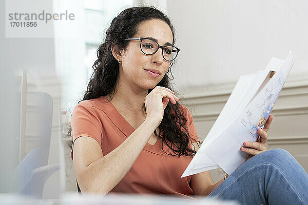 Weibliche Fachkraft liest ein Dokument,  während sie im Büro sitzt