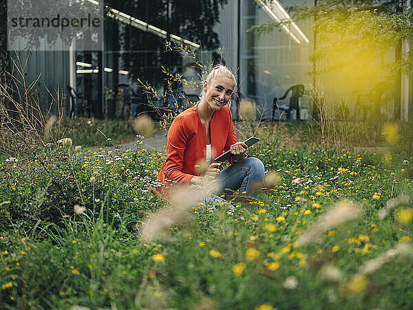 Glückliche Unternehmerin mit digitalem Tablet im Bürogarten