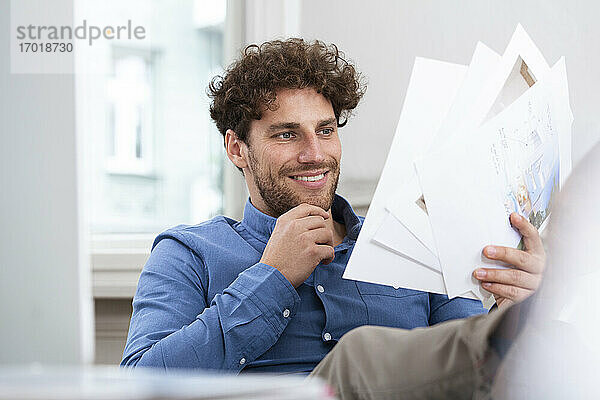 Lächelnder Geschäftsmann mit Hand am Kinn beim Lesen eines Dokuments im Büro