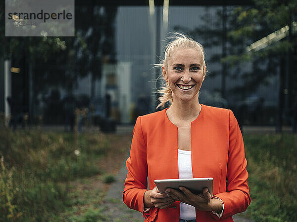 Glückliche Geschäftsfrau mit digitalem Tablet im Firmengarten