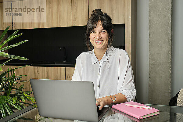 Porträt einer jungen Frau,  die zu Hause am Laptop arbeitet