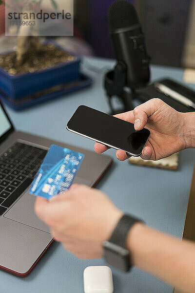 Geschäftsmann mit Kreditkarte beim Einkaufen über das Mobiltelefon zu Hause