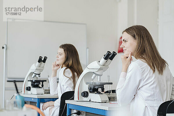 Blick von hinten auf junge Forscher in weißen Kitteln in einer wissenschaftlichen Klasse