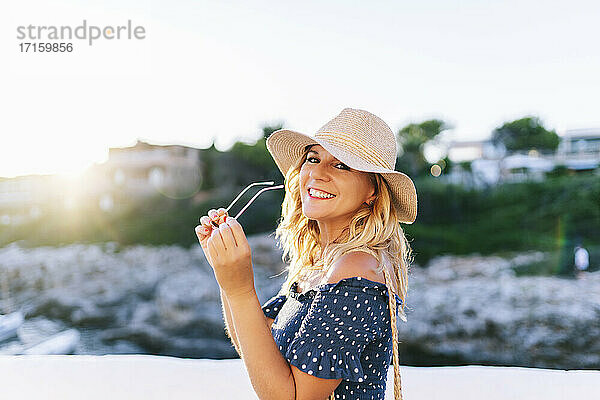 Lächelnde,  schöne Frau mit Sonnenbrille vor einem klaren Himmel im Dorf Binibeca,  Menorca,  Spanien