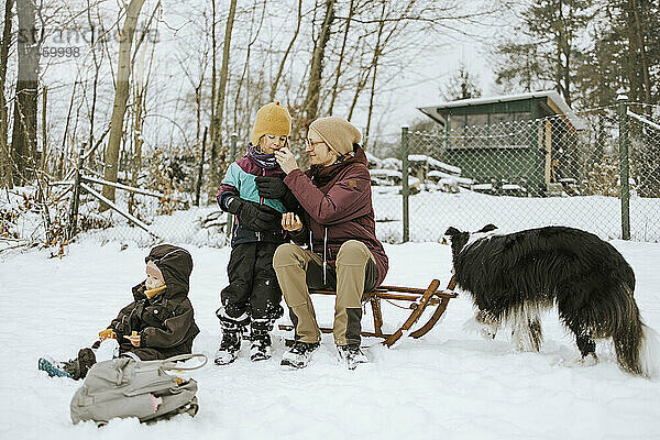 Mutter,  die ihre Tochter füttert,  während sie im Winter im Schnee ein Wochenende mit der Familie verbringt