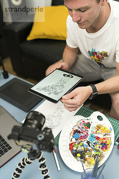 Künstler schaut auf ein digitales Tablet,  während er zu Hause über einen Laptop live streamt