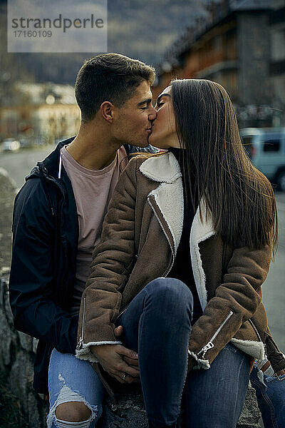 Junges Paar,  das sich mit geschlossenen Augen küsst,  während es in der Stadt sitzt