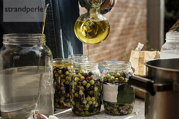 Älterer Mann gießt Olivenöl in Glasgefäß auf Tisch