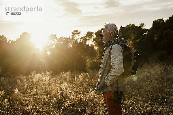 Älterer männlicher Wanderer mit Händen in den Taschen auf einem landwirtschaftlichen Feld bei Sonnenuntergang