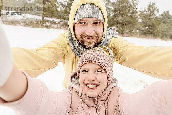 Nahaufnahme eines lächelnden Vaters und einer lächelnden Tochter in einer verschneiten Landschaft