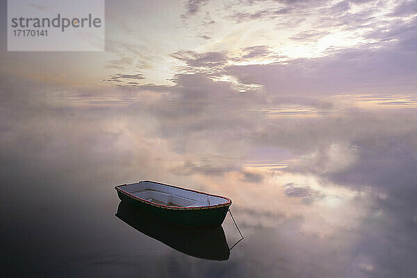 Boot vertäut auf ruhiger See gegen bewölkten Himmel bei Sonnenuntergang