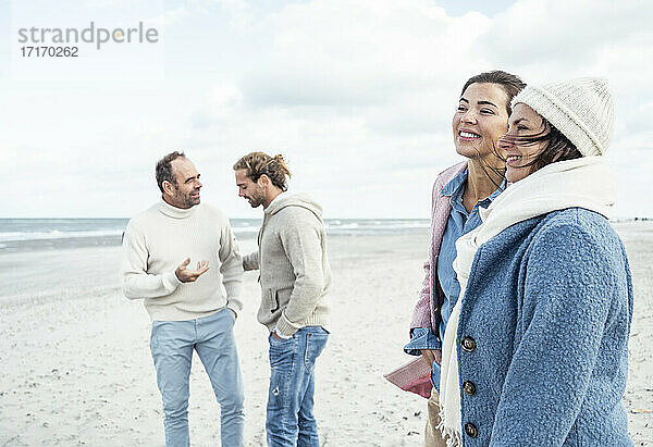 Gruppe erwachsener Freunde,  die am Küstenstrand stehen und sich unterhalten