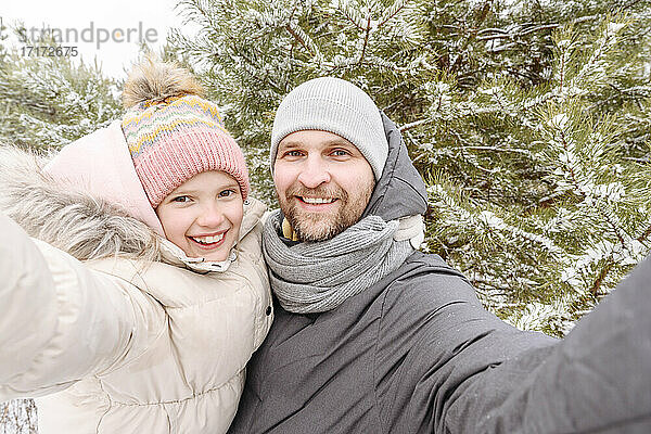 Lächelnder Vater und lächelnde Tochter gegen Bäume im Wald im Winter