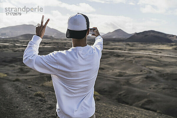 Junger männlicher Tourist gestikuliert friedlich,  während er ein Selfie am Vulkan El Cuervo macht,  Lanzarote,  Spanien,  im Urlaub