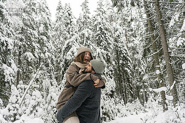 Junger Mann,  der eine Frau auf dem Arm trägt,  während er im Wald steht