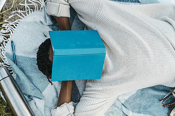 Junger Mann hält ein Nickerchen und bedeckt sein Gesicht mit einem Buch