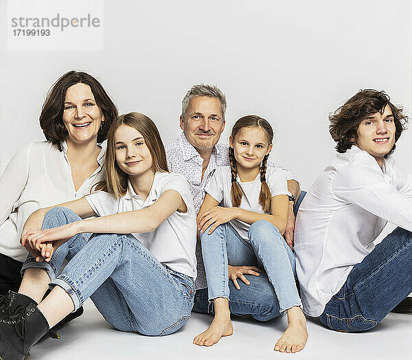 Familie mit Kindern sitzend vor weißem Hintergrund