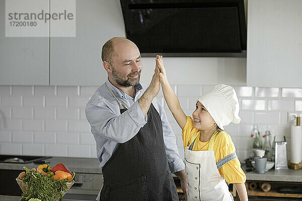Lächelnder Vater und lächelnde Tochter geben sich in der Küche fünf