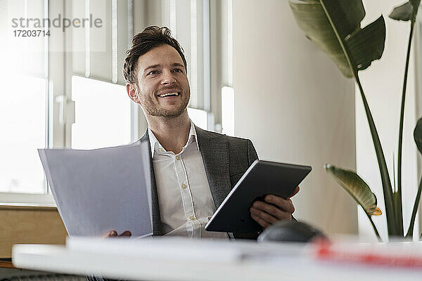 Glücklicher Geschäftsmann mit digitalem Tablet und Dokument im Büro