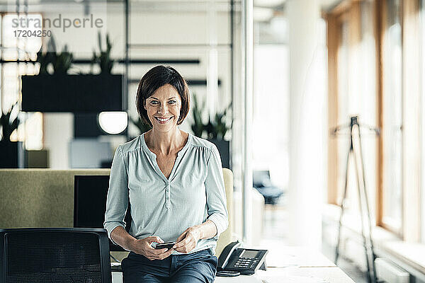 Glückliche Geschäftsfrau mit Smartphone im Büro
