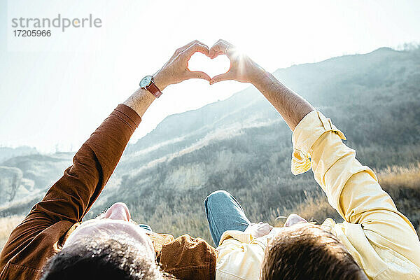 Homosexuelles Paar macht Herzform mit Händen vor einem Berg