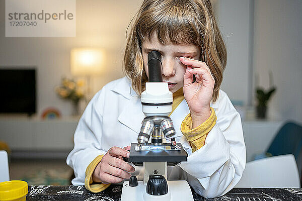 Mädchen im Laborkittel schaut zu Hause durch ein Mikroskop