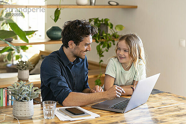 Lächelnder Vater und lächelnde Tochter schauen sich zu Hause vor dem Laptop an