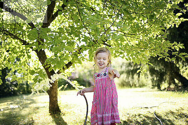 Glückliches Mädchen gestikuliert,  während sie ein Bewässerungsrohr im Garten hält