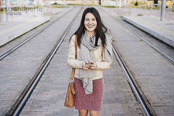 Glückliche Frau mit Smartphone inmitten von Eisenbahnschienen